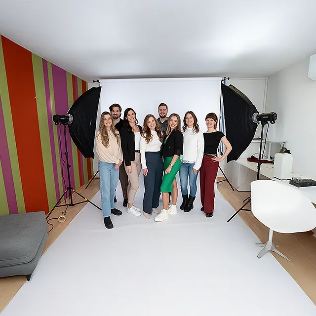 Die marketminder Julia Gorton, Viktoria Groiß, Ferdinand Schenk, Bettina Rabensteiner, Philipp Zelenka, Julia Andert, Luca Zsofia Trapp und Nataliia Karall beim On-Boarding Fotoshooting im marketmind Büro, umgeben von professionellem Equippment.