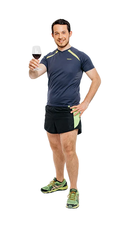 Andreas Kritsch, MSc trägt Laufkleidung und hebt mit einem Lächeln ein Glas Rotwein – eine charmante Kombination aus Ausdauerlauf und Genuss.