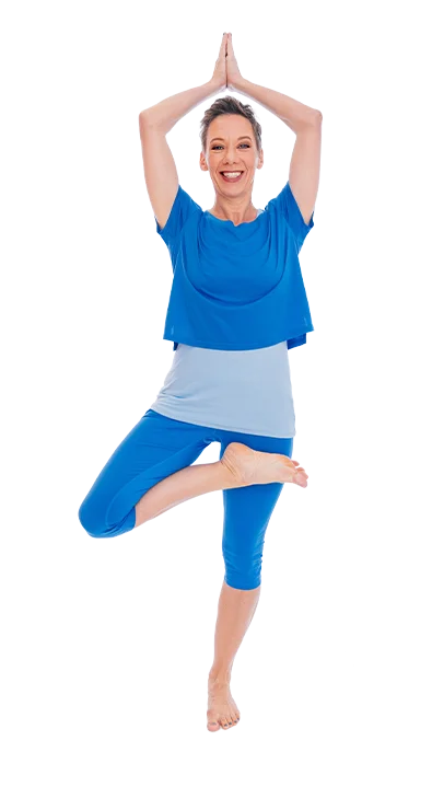 Mag. Dagmar Jiresch steht barfuß in der Baumposition und trägt ein blaues Yoga-Outfit – voller Balance, Energie und innerer Ruhe.