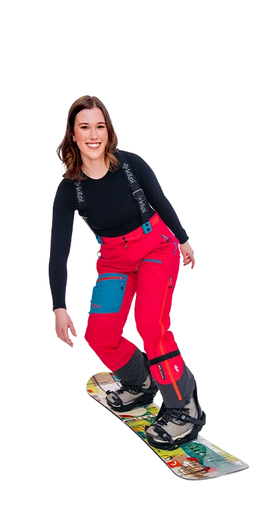 Lena Hammer, MA fährt in knallroter Skibekleidung auf einem Snowboard, lacht in die Kamera – voller Schwung und Spaß im Schnee.