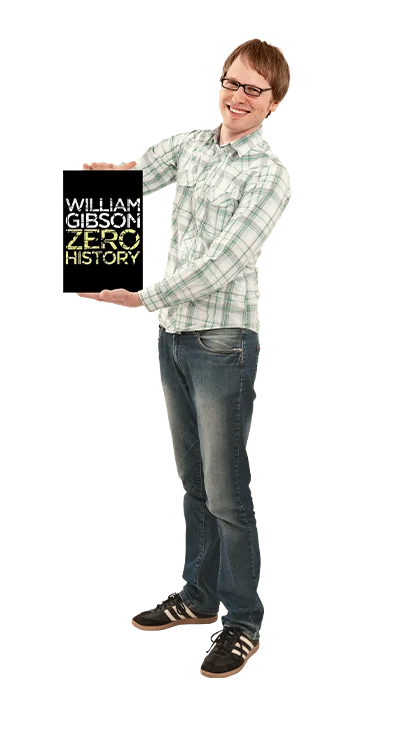 Mag. Martin Fuchs hält das Buch 'Zero History' von William Gibson in die Kamera, trägt Jeans und Sneaker – technikinteressiert, lesefreudig und mit Sinn für Sci-Fi.
