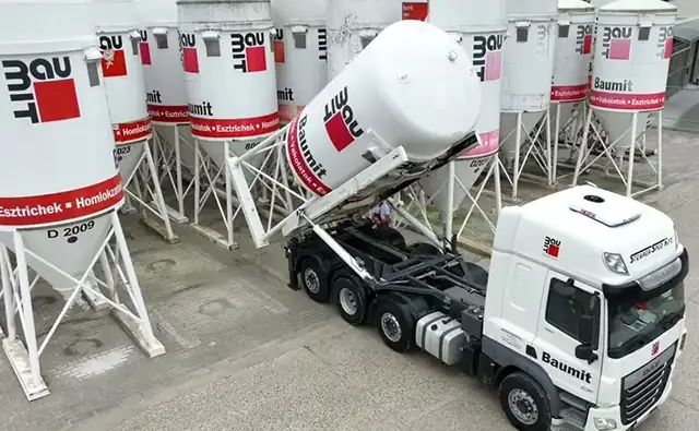 Baumit-LKW liefert einen Silobehälter auf ein Firmengelände mit mehreren Baustoffsilos.