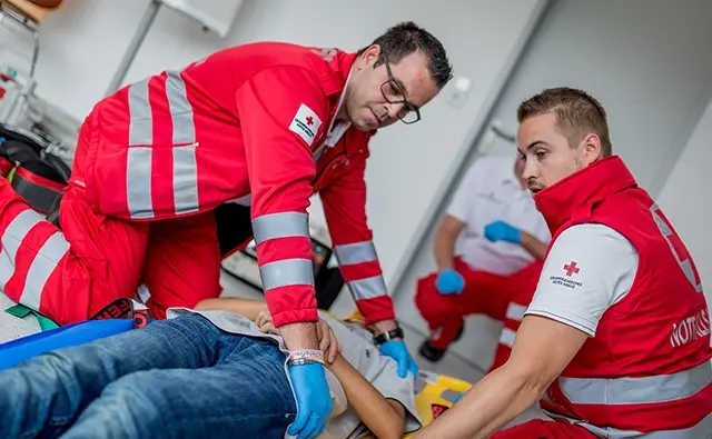 Rettungssanitäter des Österreichischen Roten Kreuzes bei einer Erste-Hilfe-Maßnahme. Bild betont den humanitären Einsatz und die medizinische Versorgungskompetenz.