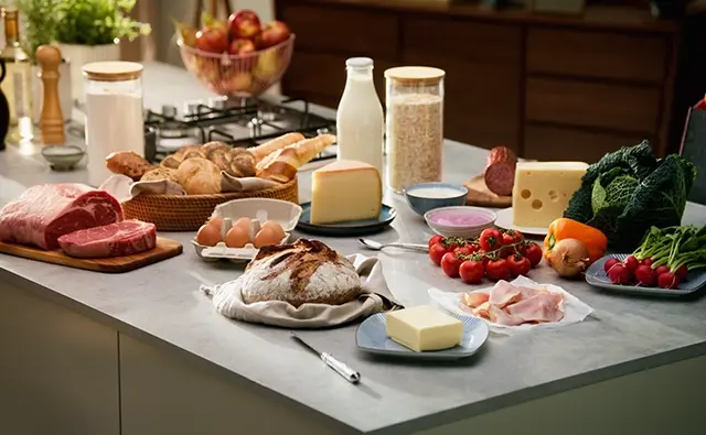 Frischwaren auf einem modernen Küchentresen, darunter regionale Produkte wie Brot, Milch, Eier, Fleisch, Gemüse und Käse. Symbolbild für AMA-Marketingkampagnen zur Qualität und Herkunft österreichischer Lebensmittel.