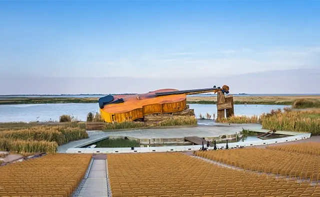Aussergewöhnliche Bühnenkulisse am Neusiedler See mit überdimensionalem Chellomodell. Symbolbild für die kreative Inszenierung und internationale Anziehungskraft der Seefestspiele Mörbisch.