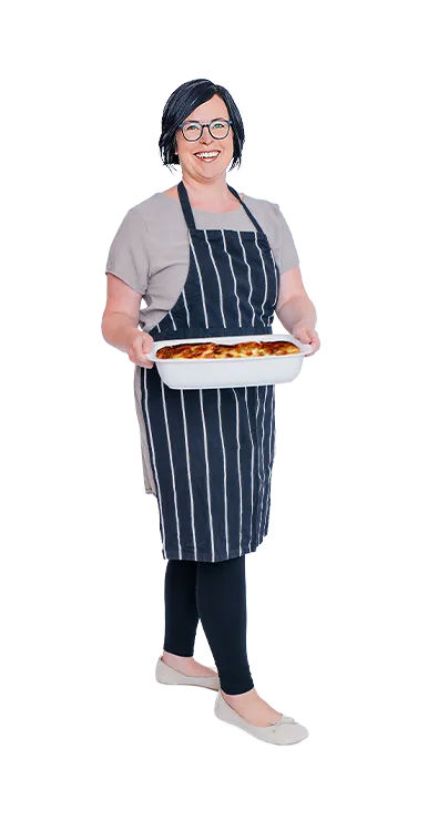 Mag. Anita Salamon trägt eine gestreifte Schürze und hält stolz ein frisch gebackenes Auflaufgericht in den Händen - herzlich, genussfreudig und mit Freude am Kochen.