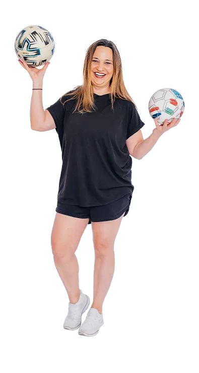Mag. Birgit Hütter steht lächelnd in Sportoutfit und hält zwei Fussbälle in den Händen - aktiv, spielerisch und voller guter Laune.
