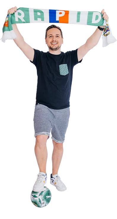 Matthias Obermeier, MSc jubelt mit einem Fussballschal und balanciert einen Ball am Fuss - sportlich, energiegeladen und voller Teamgeist.