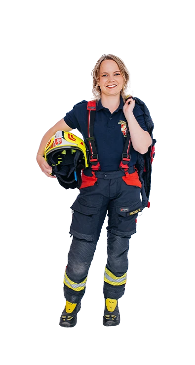 Nadine Buchta, MA trägt eine dunkelblaue Feuerwehr-Einsatzhose mit roten Hosenträgern und gelben Reflexstreifen, den Feuerwehrhelm unter dem Arm und die Einsatzjacke über der Schulter - mit Leidenschaft bei der freiwilligen Feuerwehr.